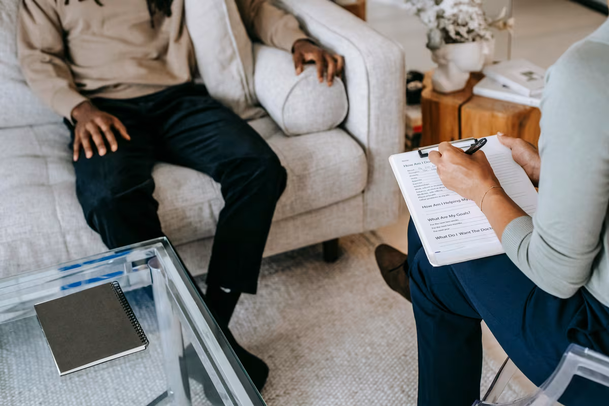 A therapist taking notes on a clipboard while a client sits on a sofa during a session