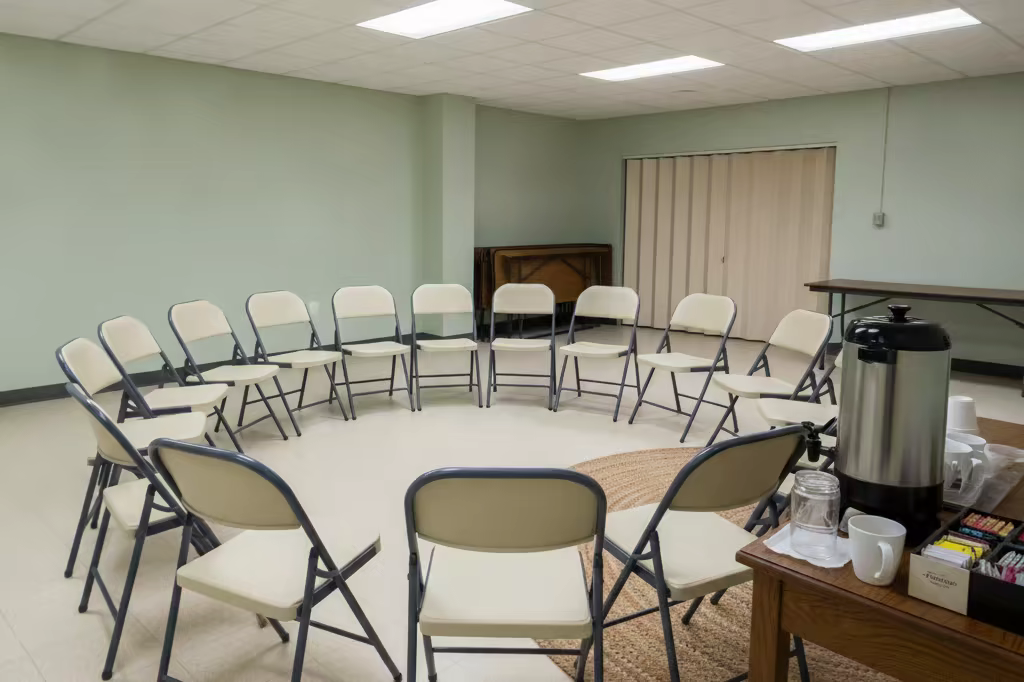 A folding chair circle set up in a church basement meeting room before people arrive