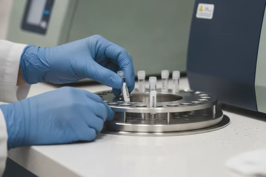 A laboratory technician's gloved hands placing sample tubes into an analyzer tray