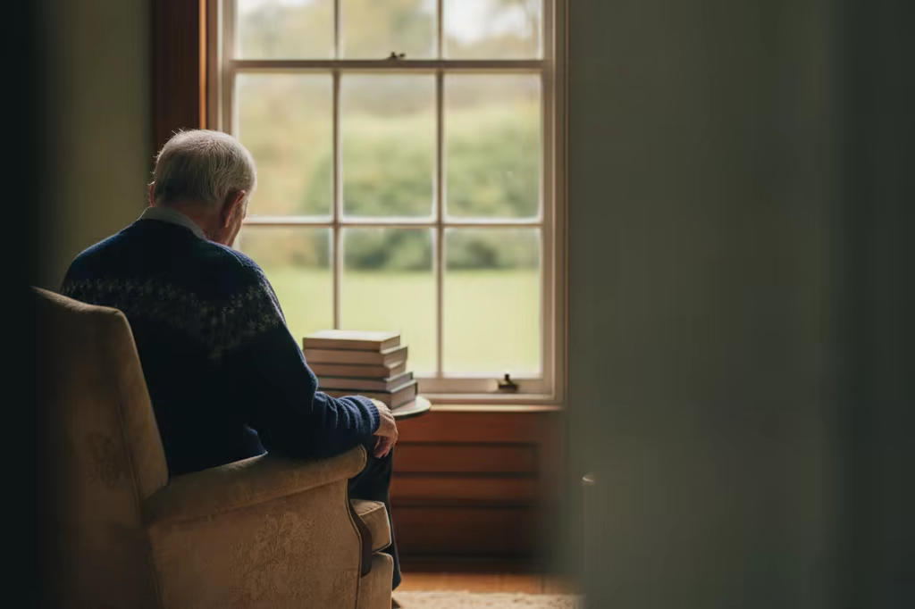 An older man seated by a window in soft light, photographed from behind